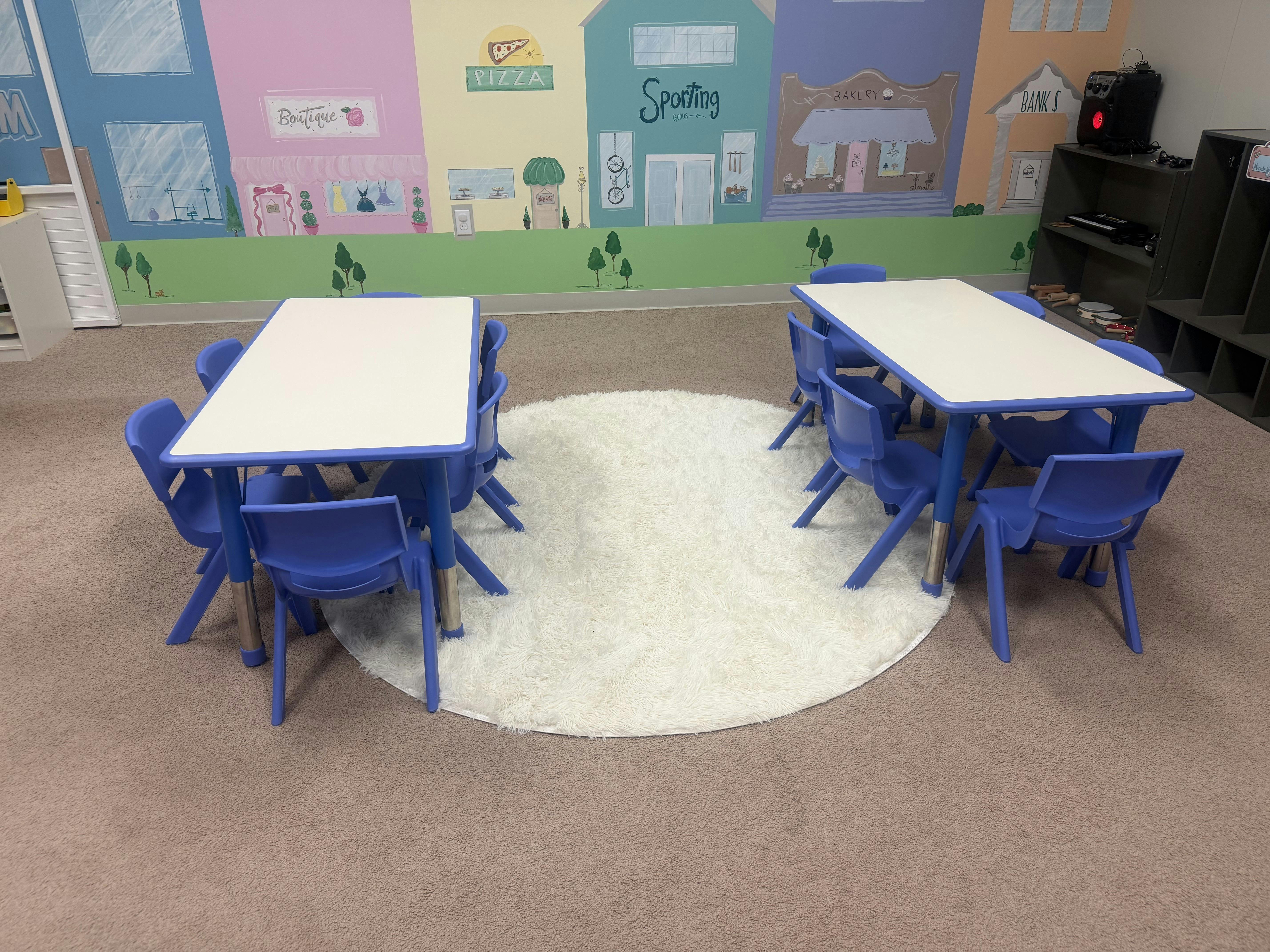 Classroom with two tables and chairs on a round white rug, murals of town stores