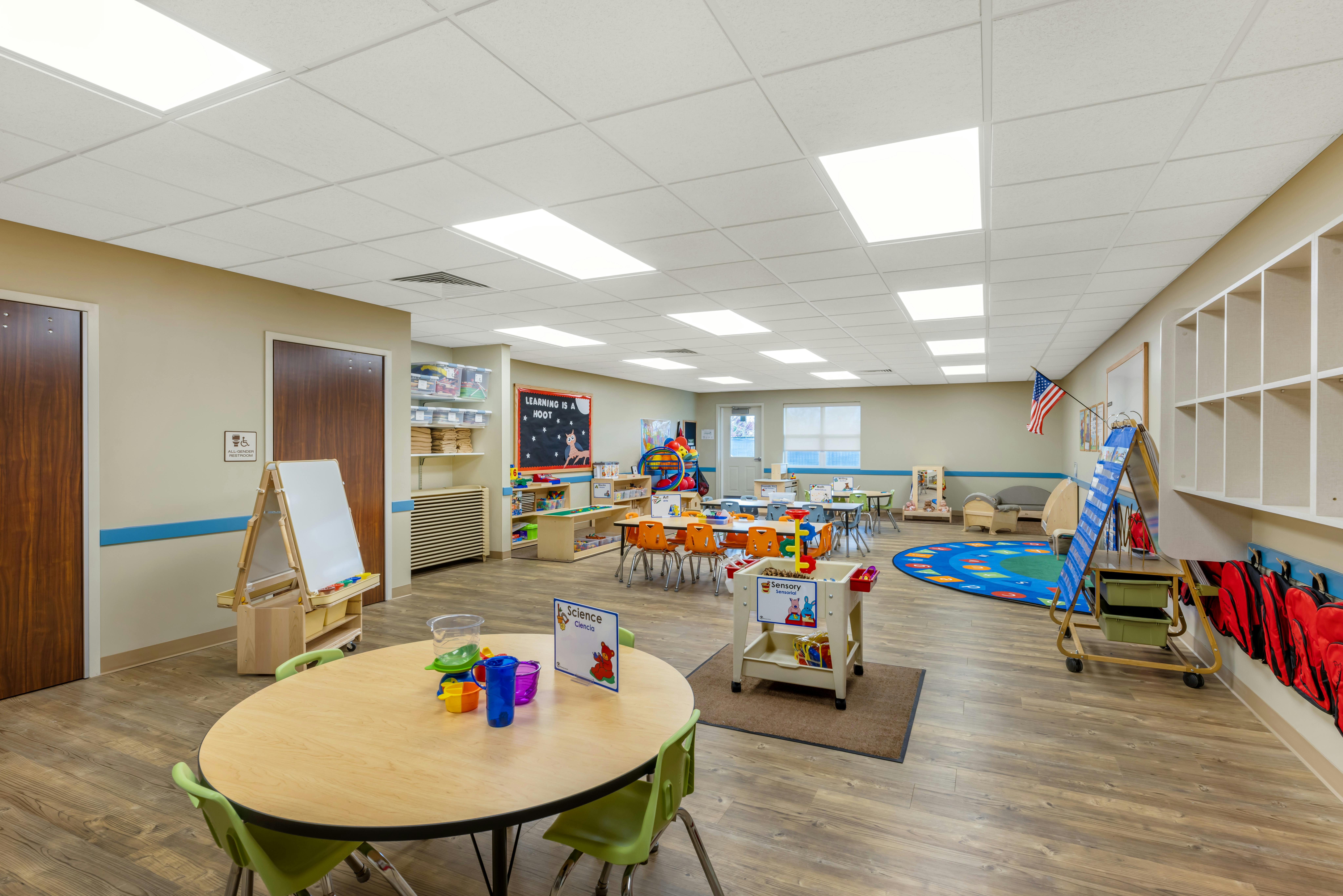 Classroom with small tables and chairs, a play rug, and storage for toys