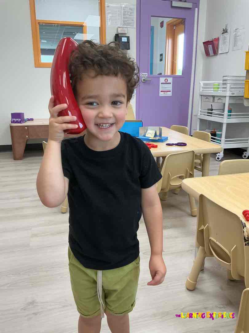 Child holding a red toy phone to their ear in a classroom
