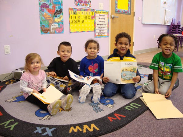 Five children sitting on a rug in a classroom, reading books