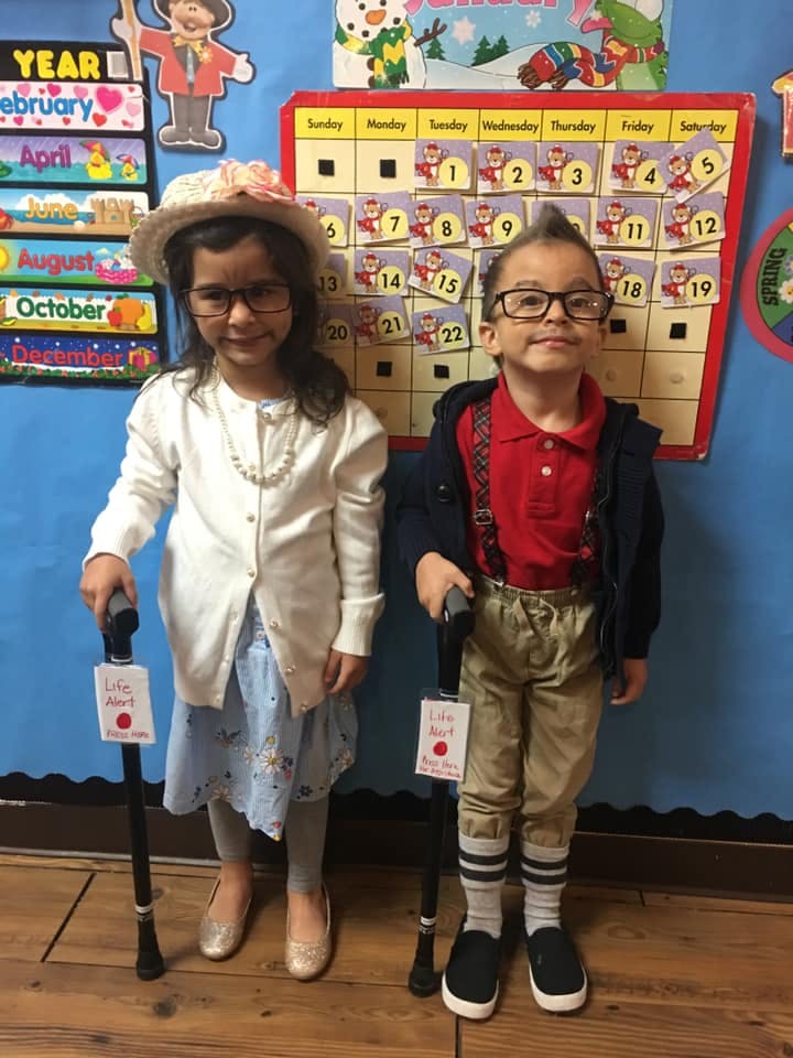 Two children dressed as older people, holding canes, in a classroom