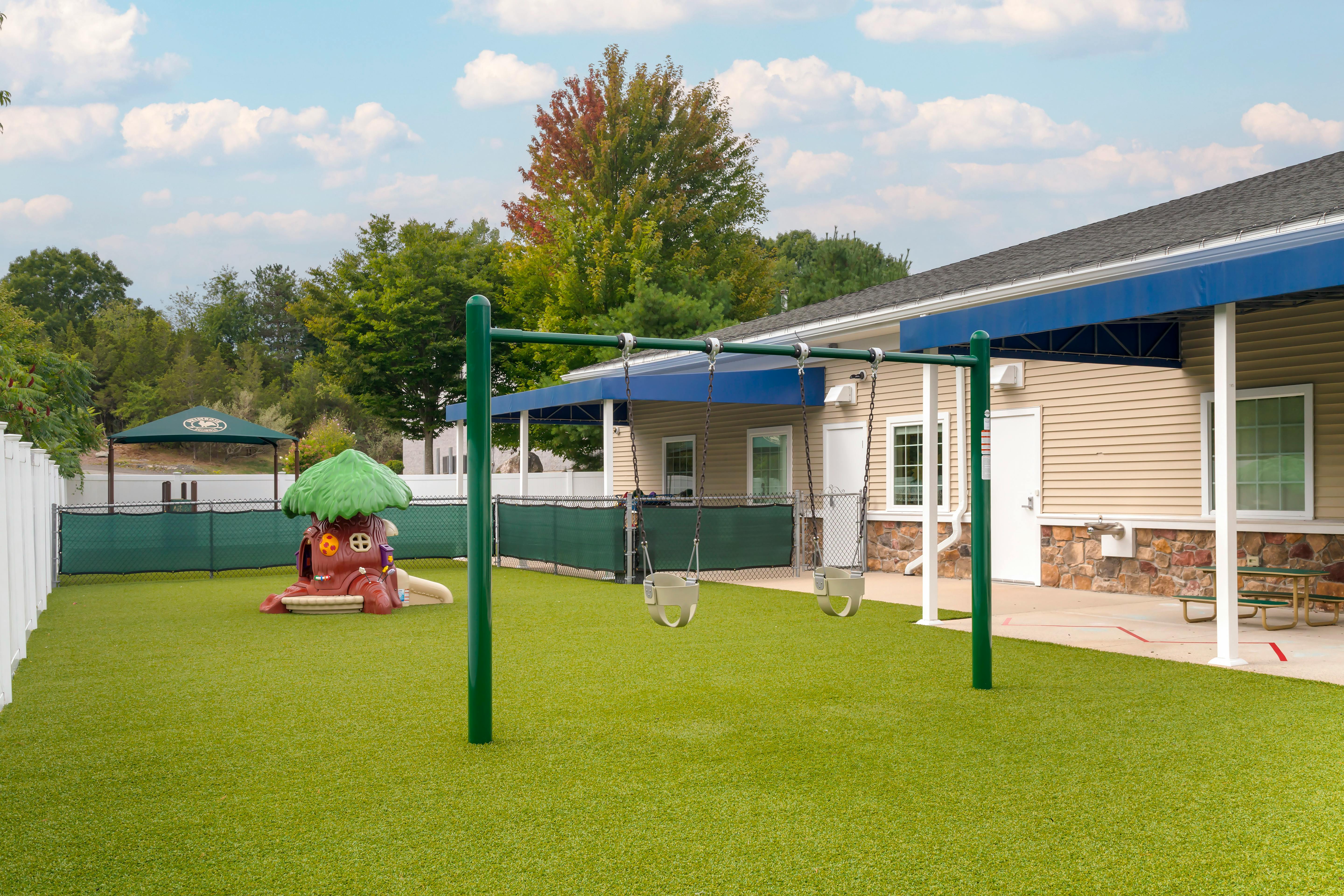 Playground with swings, a playhouse, and a picnic table on artificial turf