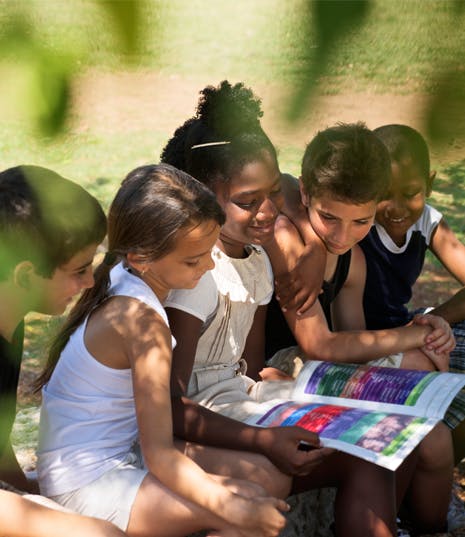 Group of children looking at a book together outdoors