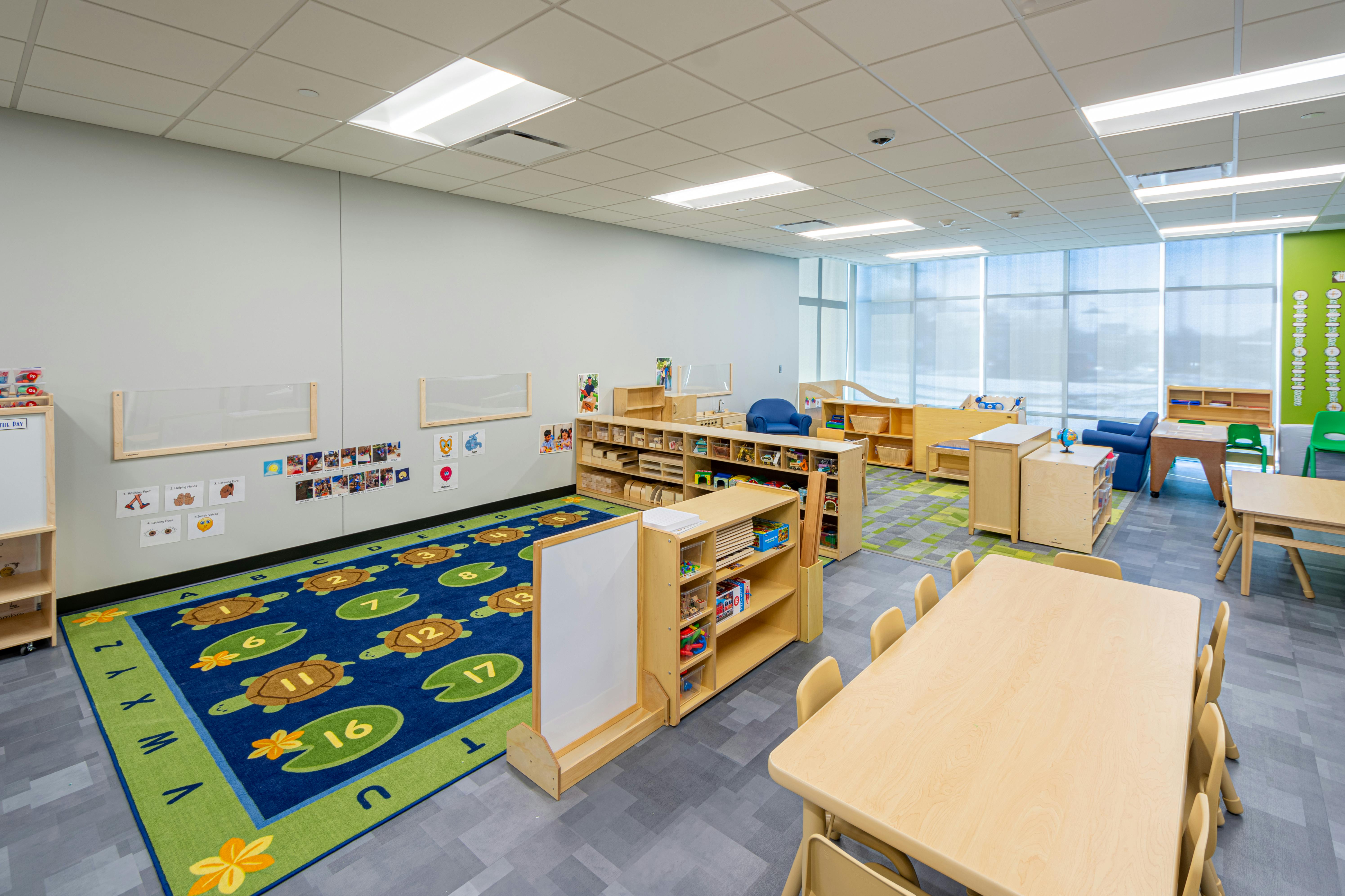 Classroom with a blue and green rug, wooden shelves, and tables