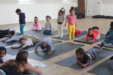 Children and adults doing yoga poses on mats in a room