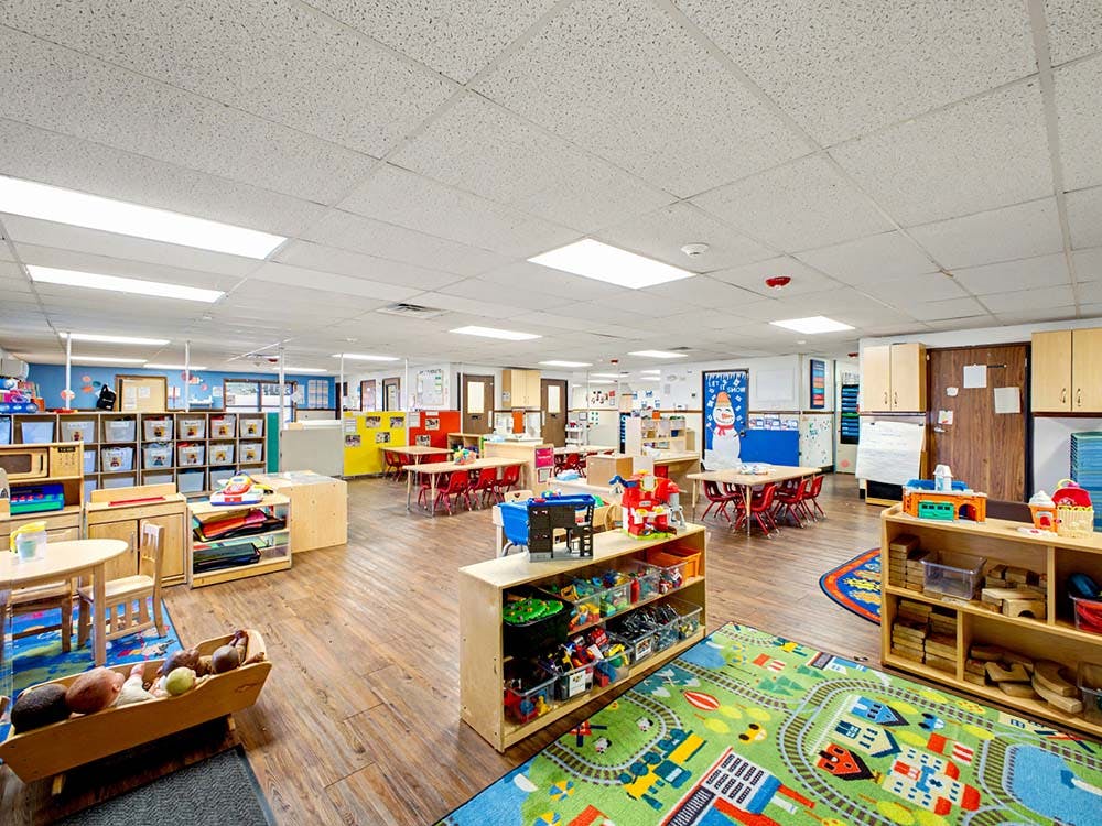 Empty classroom with small tables and chairs, shelves with toys and books