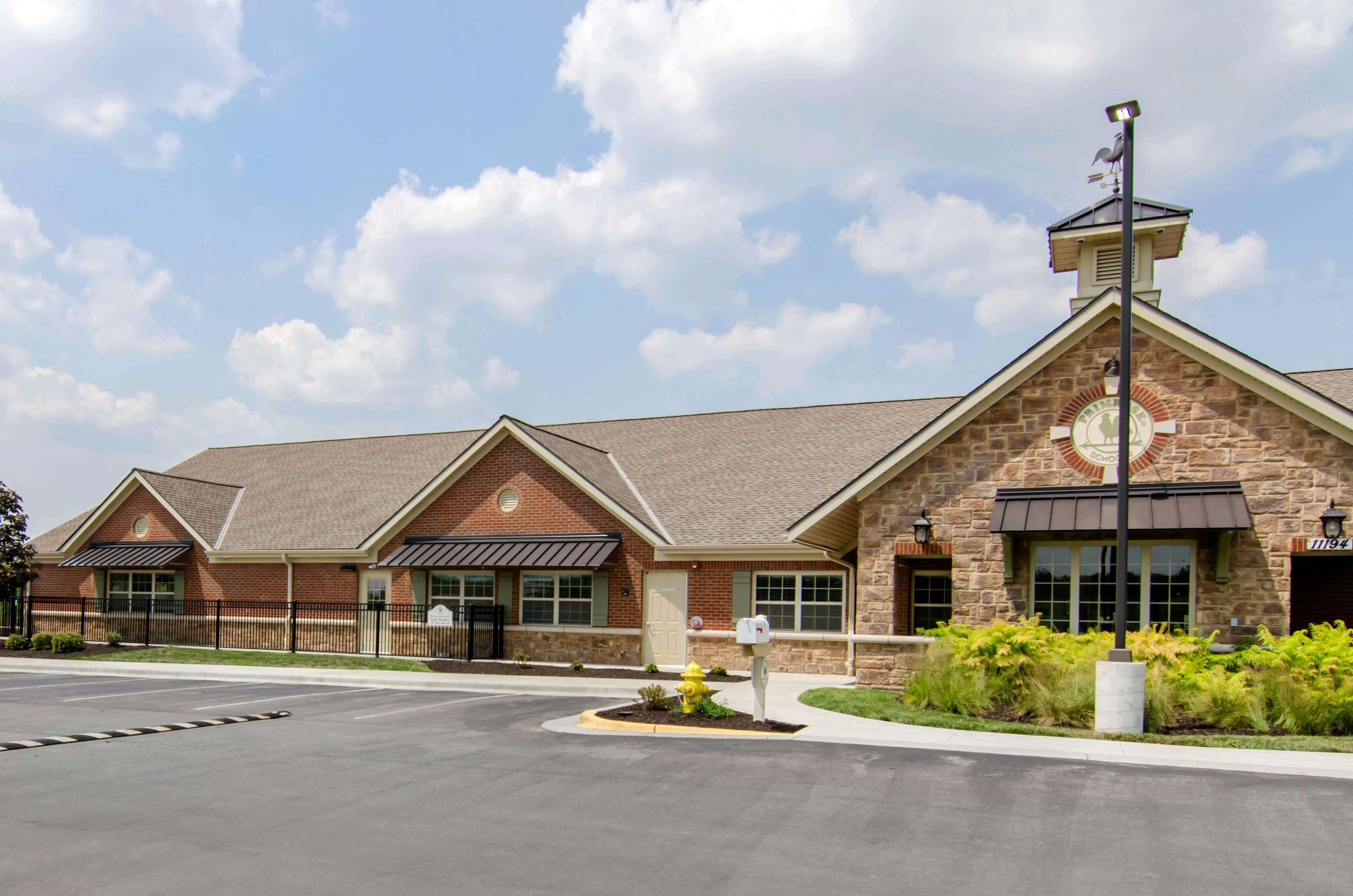 Brick and stone building with a small cupola and weather vane, a parking lot in front