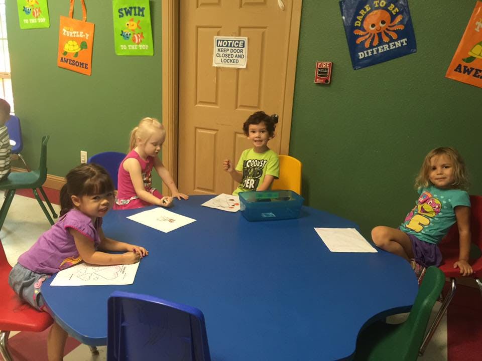 Four children sitting at a blue table with papers