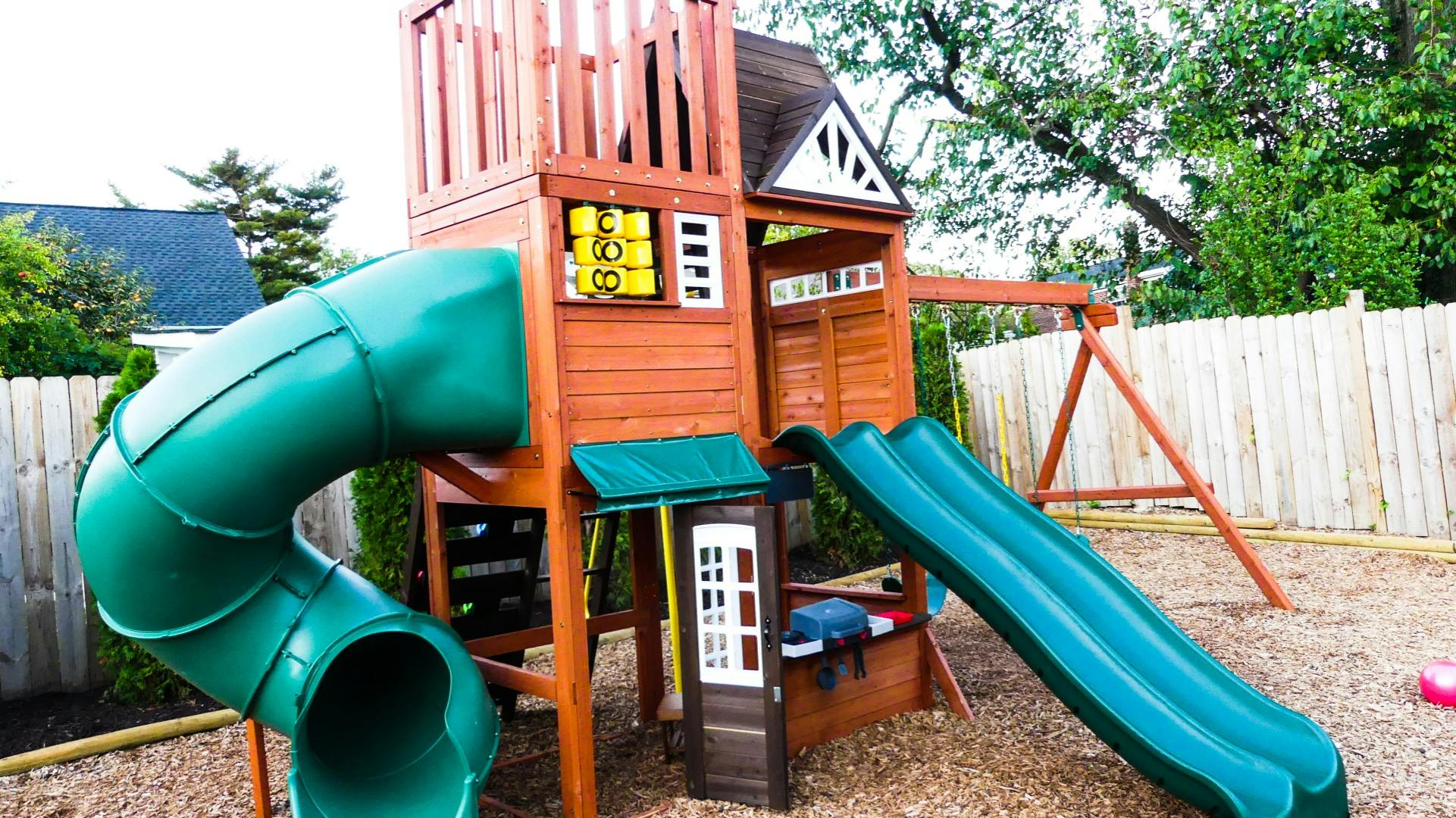 Wooden playground set with two green slides and a swing set