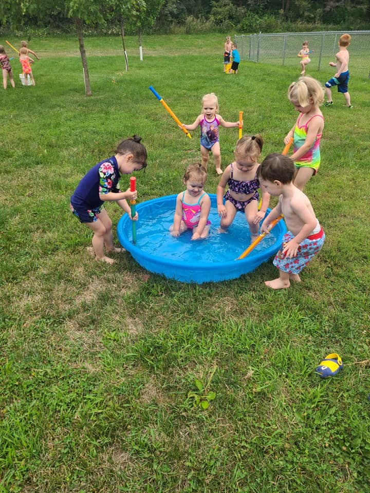 Children playing in and around a small blue wading pool outdoors