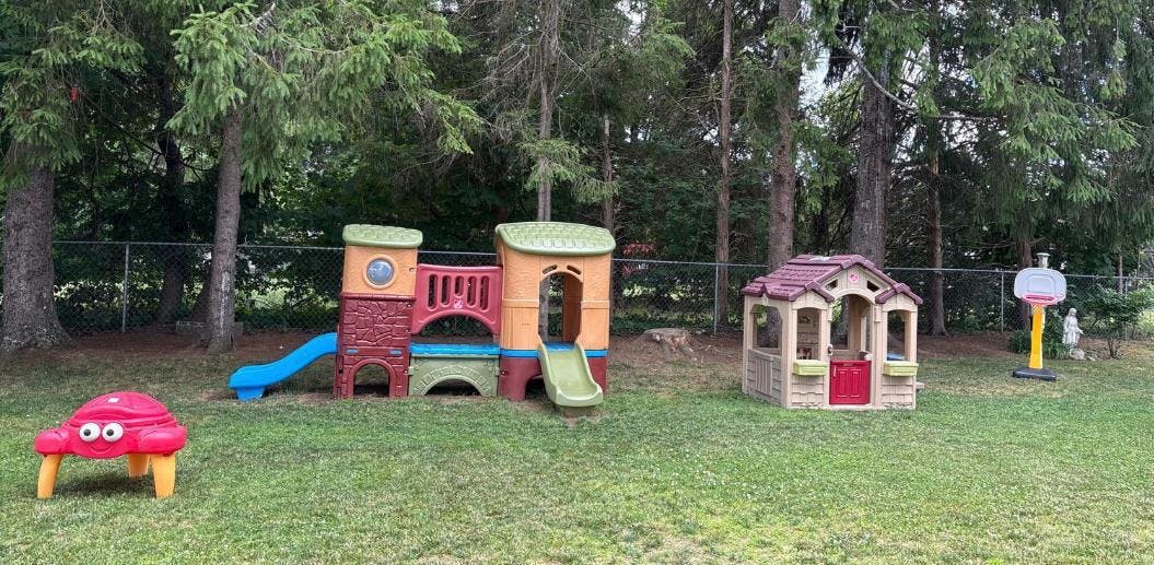 Plastic playground equipment and a small toy house on a grassy lawn