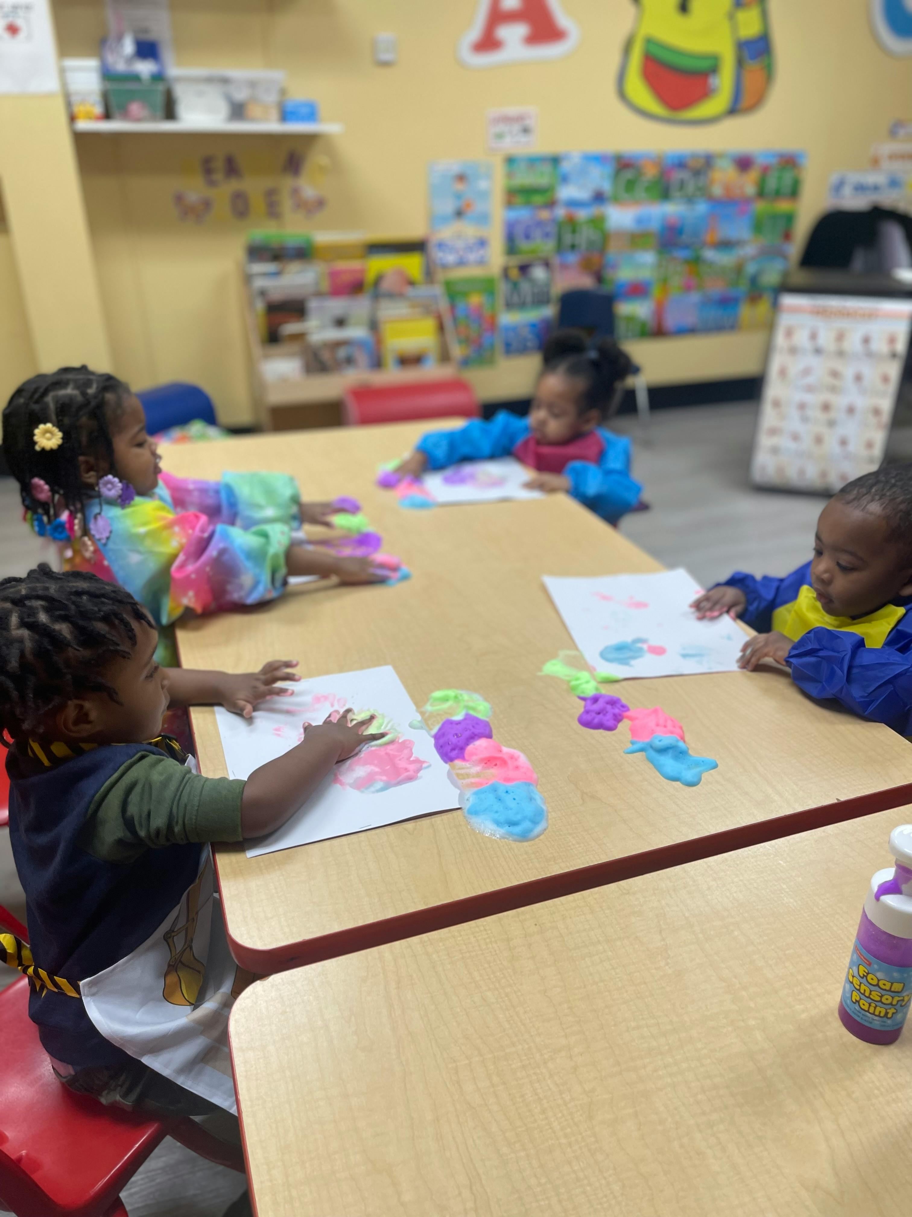 Three children at a table doing an art activity with colorful pom-poms