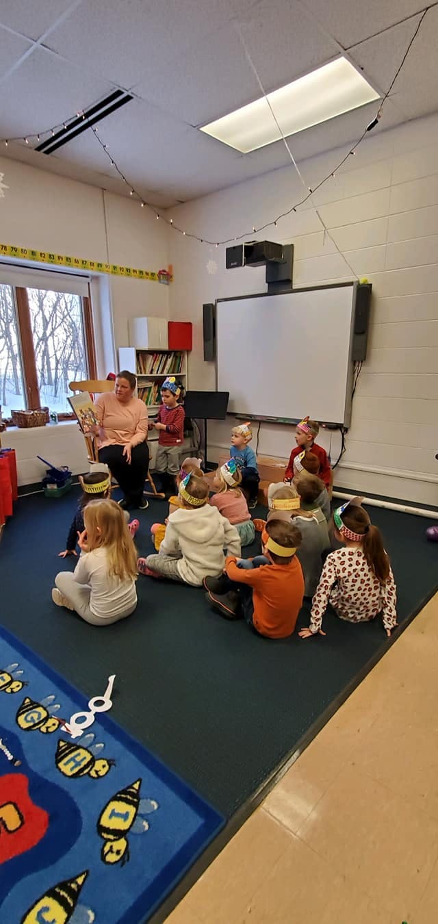 Person reading a book to a group of children in a classroom