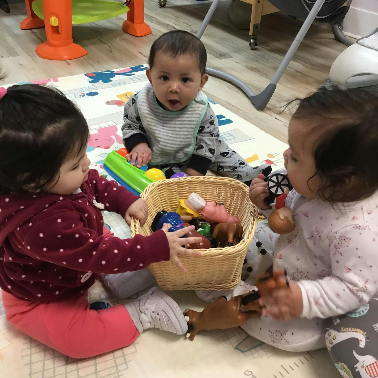 Three children playing with toys from a basket on a mat