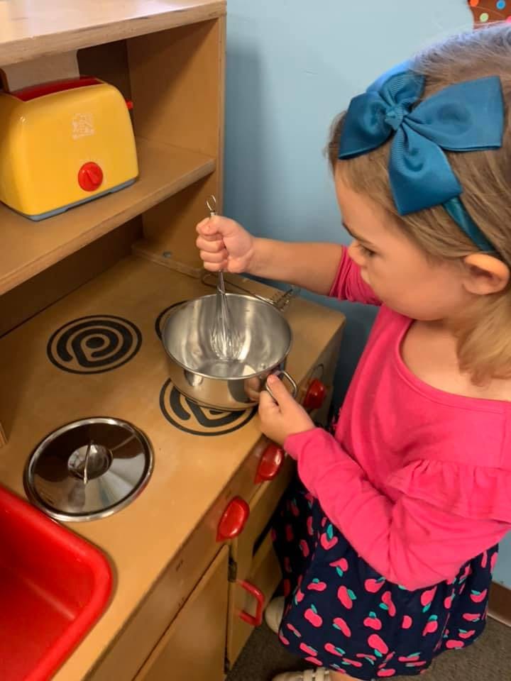 Child playing with a toy kitchen, stirring a pot with a whisk