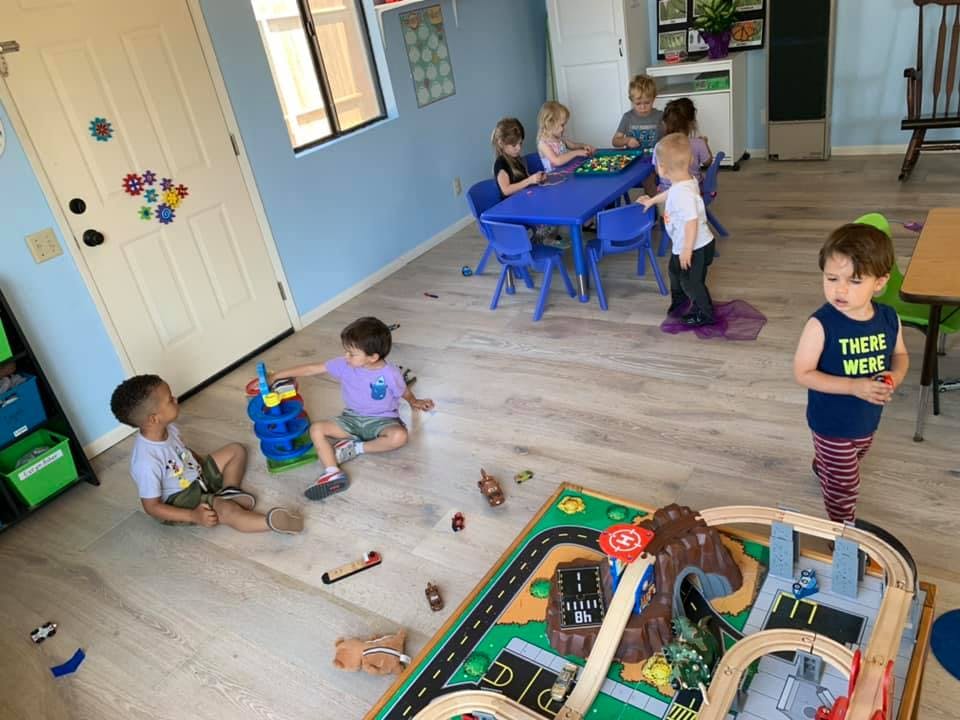 Children playing with toys in a room, some at a table and some on the floor