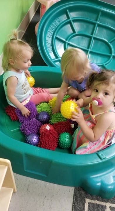 Three children playing with textured balls in a green plastic container