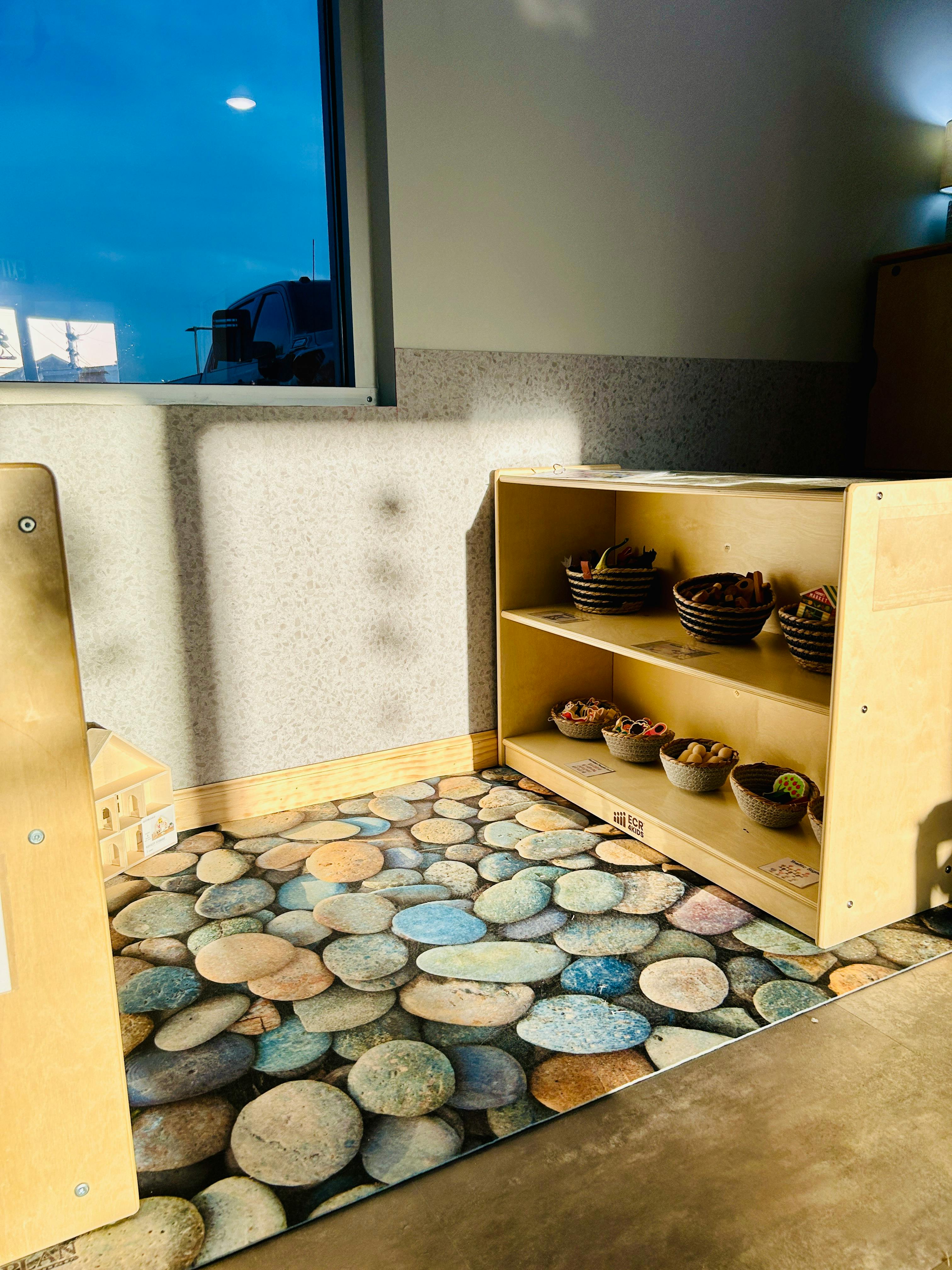 A room with a window, a wooden shelf with bowls, and a pebble-patterned rug