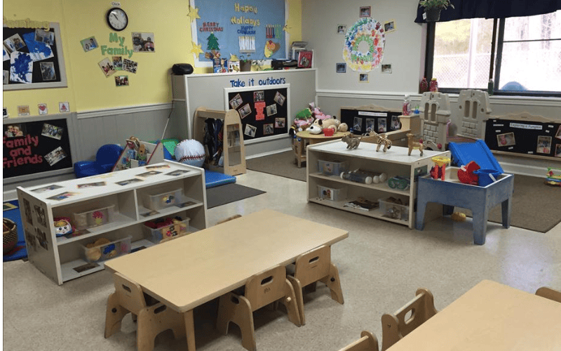Classroom with small tables and chairs, shelves with toys, and decorated walls