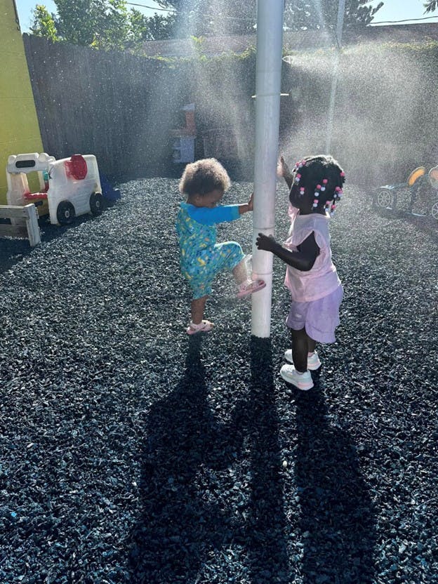 Two children playing with a water mister on a playground