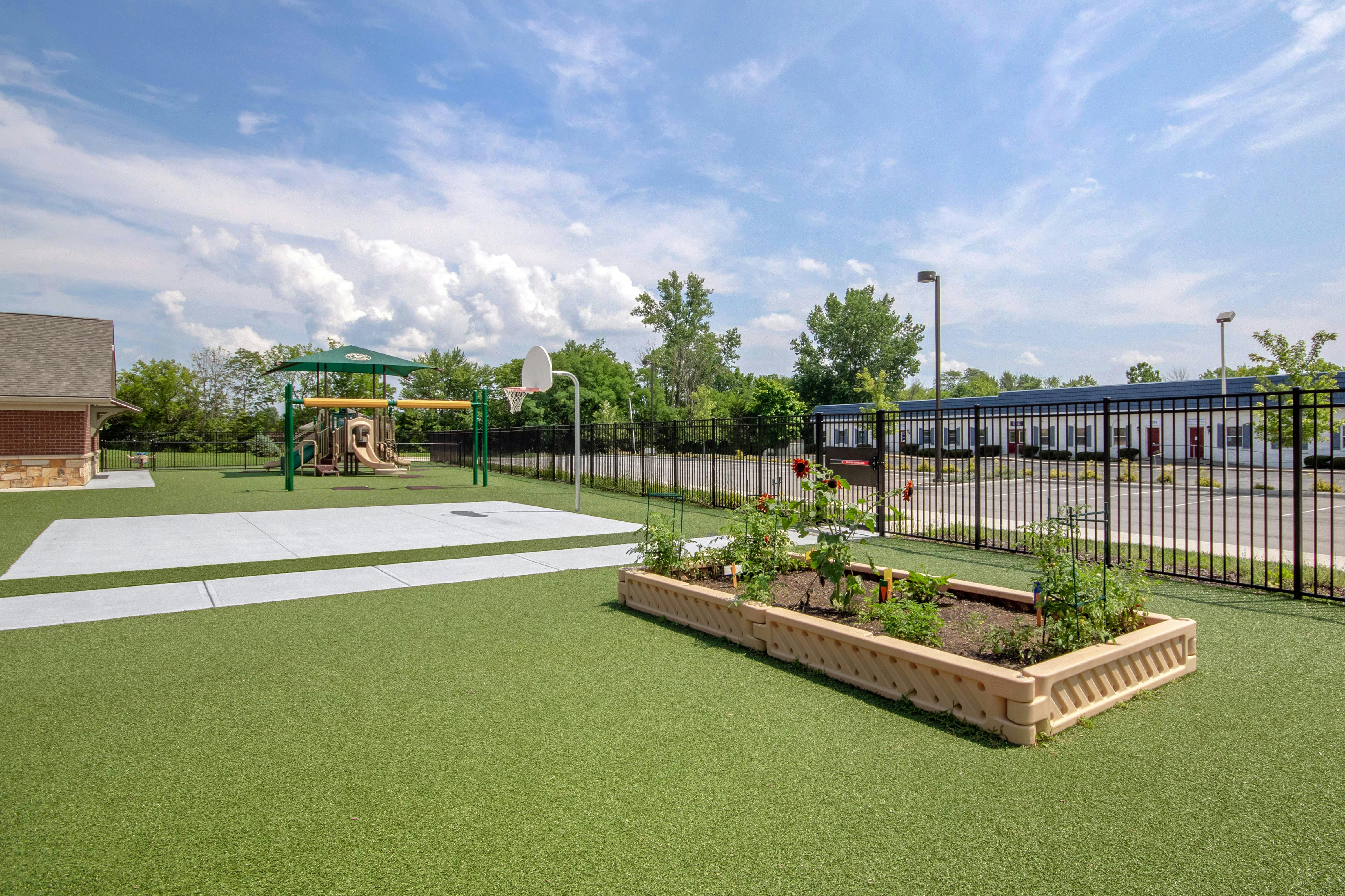 Playground with green turf, a basketball hoop, and a raised garden bed