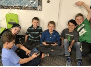 Six children sitting on the floor looking at tablets