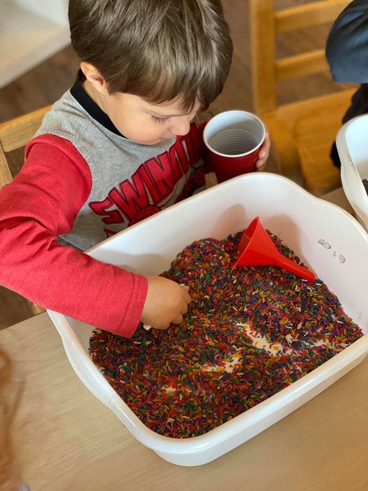 Child playing with colorful rice in a white bin