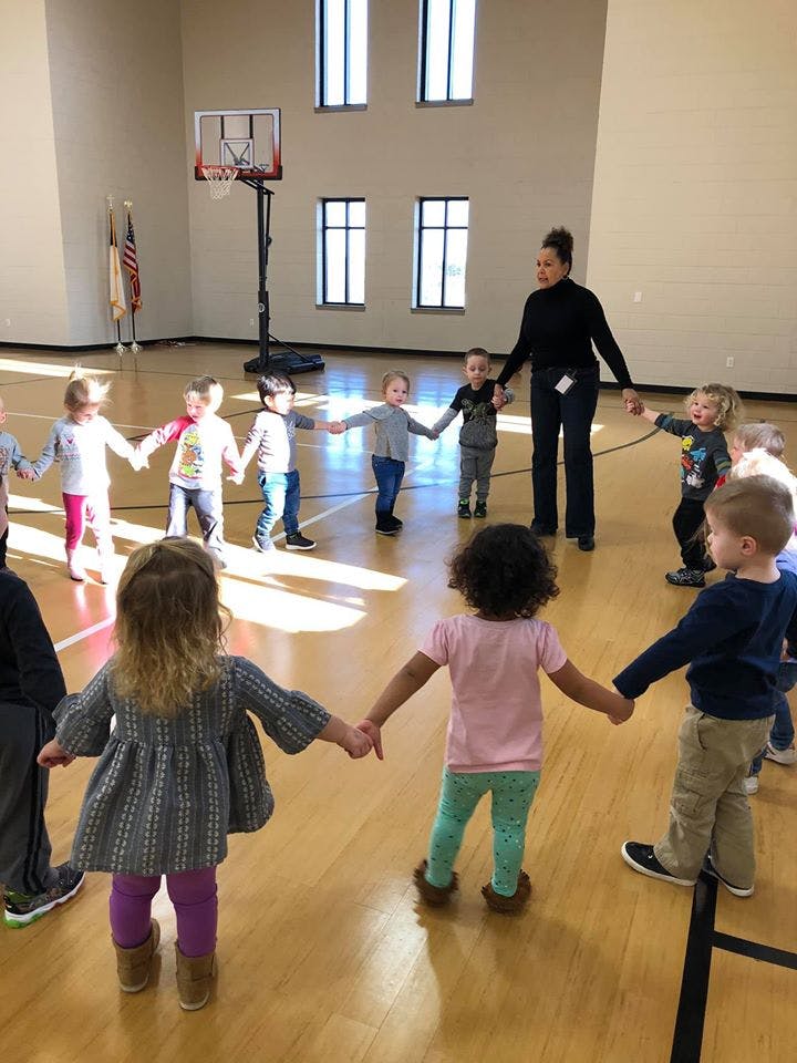 Adult and children holding hands in a circle in a gym