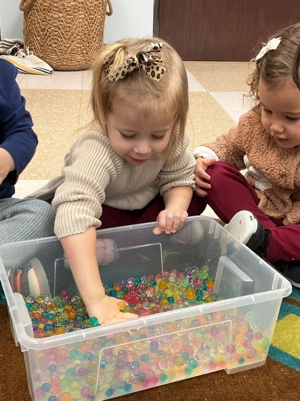 Child playing with colorful water beads in a clear bin