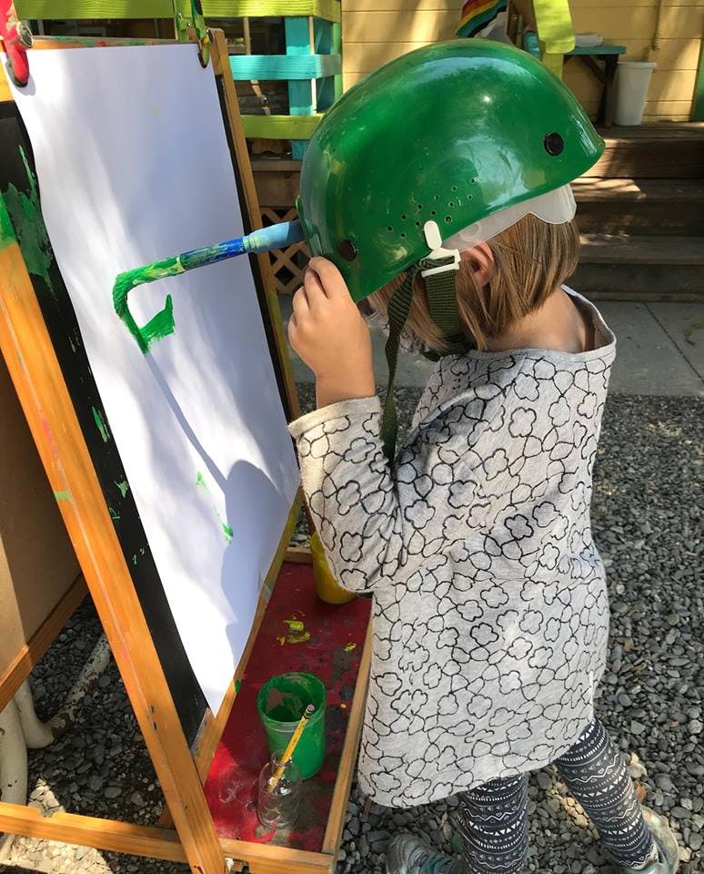 Child wearing a green helmet painting on an easel
