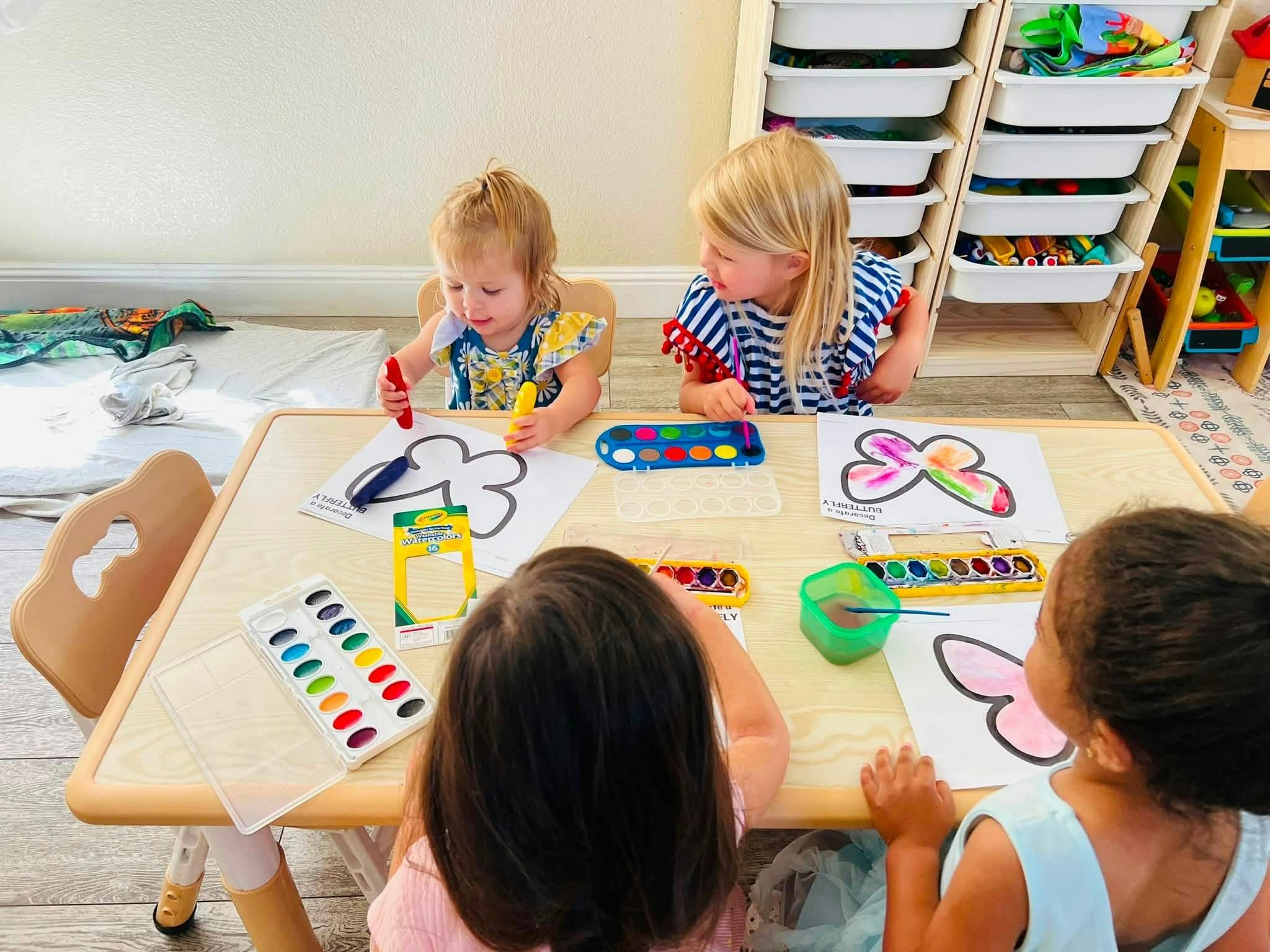 Four children painting butterfly drawings with watercolors at a table