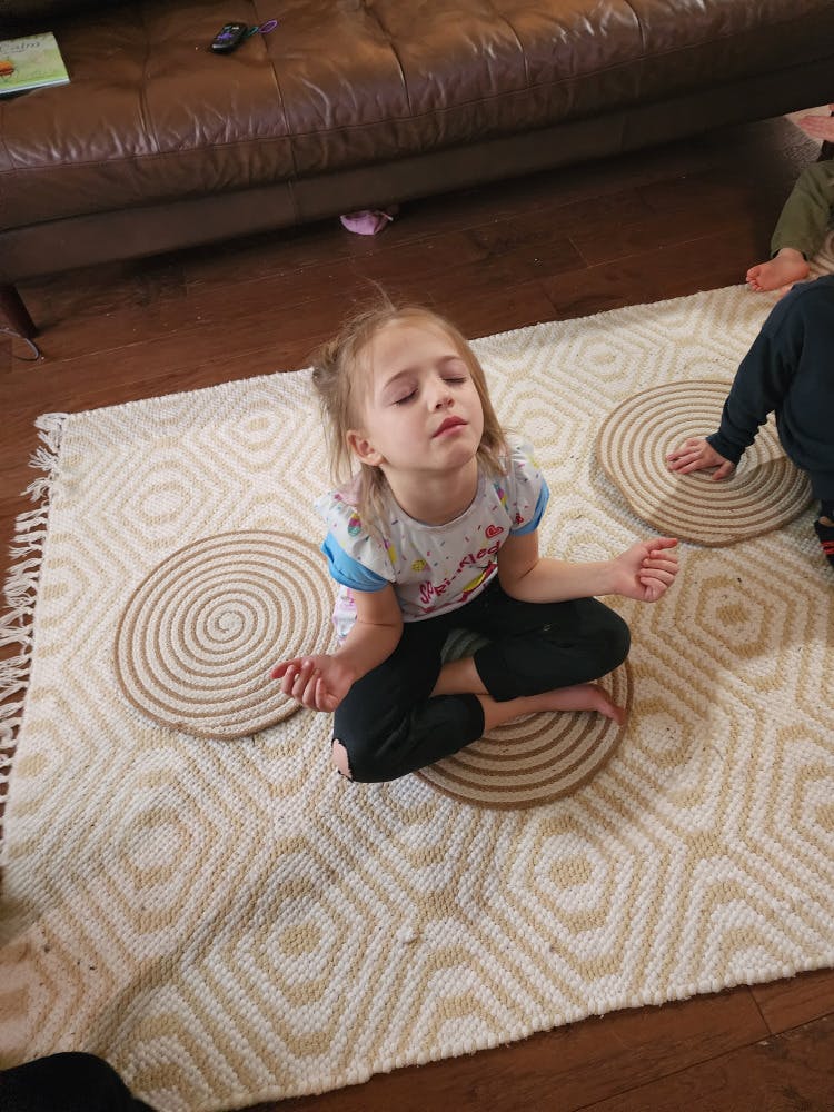 Child sitting cross-legged on a rug with eyes closed in a meditation pose