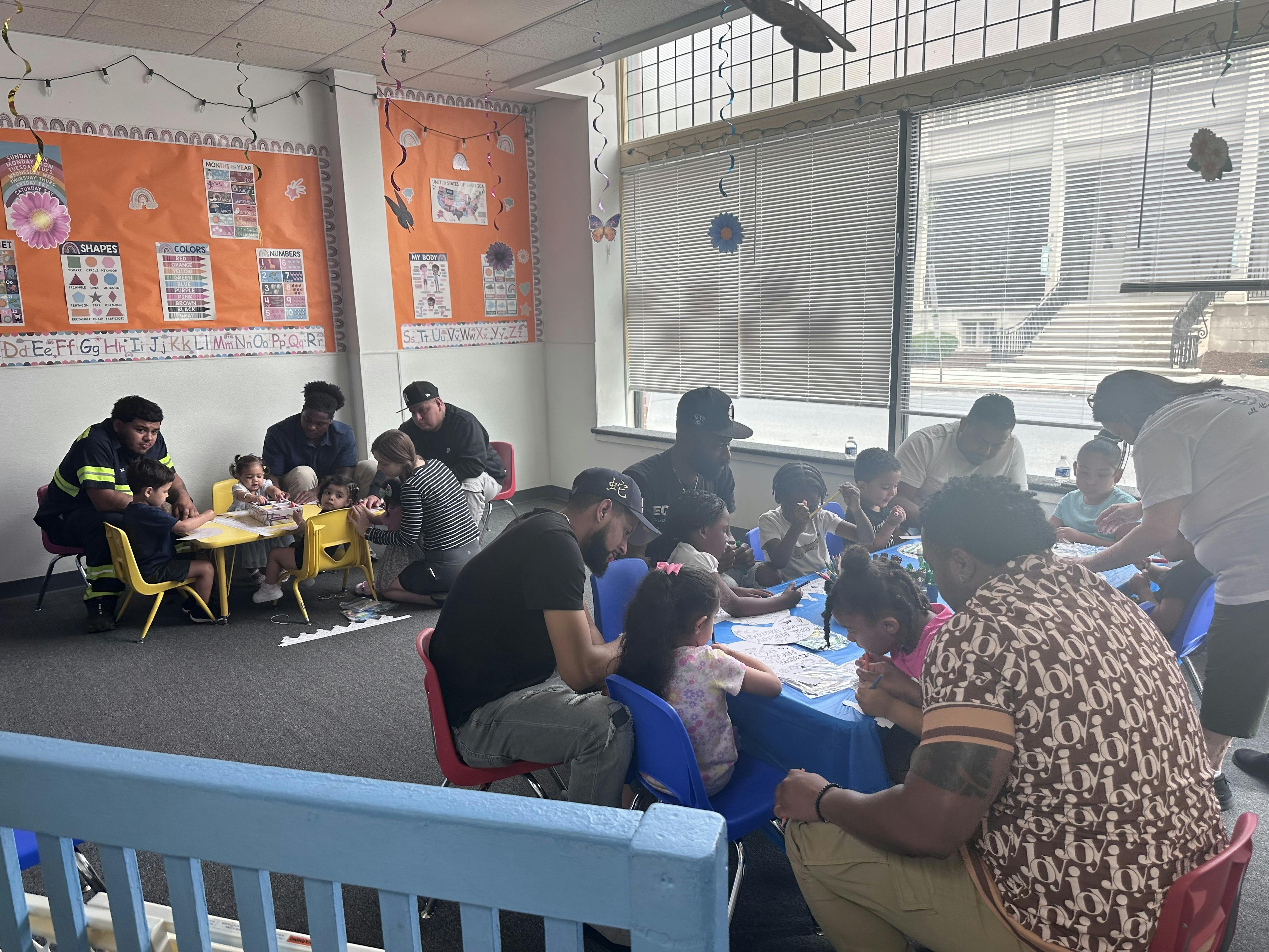 Adults and children gathered around tables in a classroom