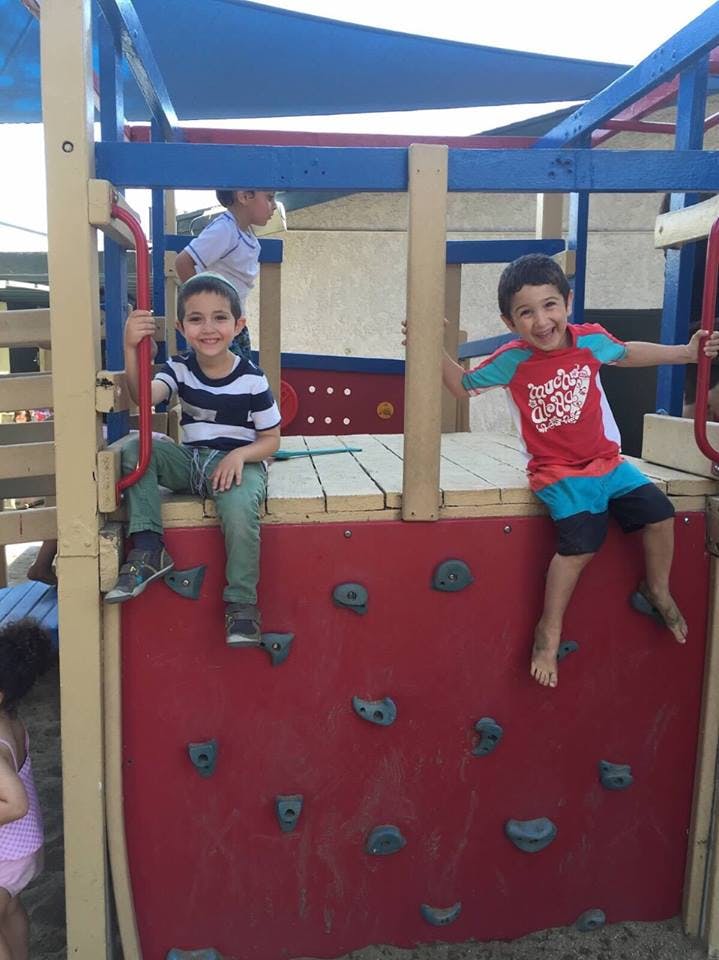 Two children on a playground structure, one sitting, one climbing