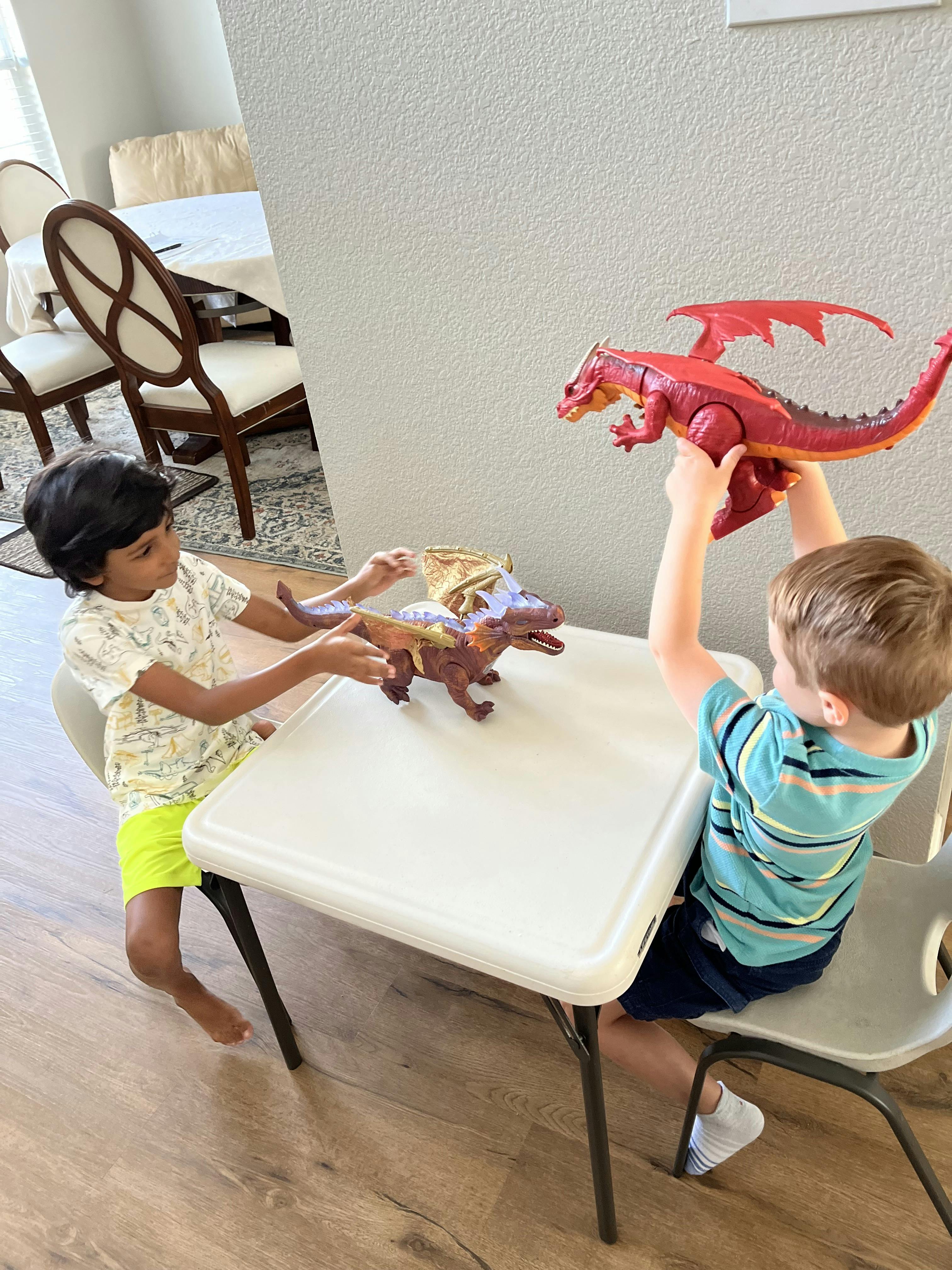 Two children playing with toy dragons at a small table