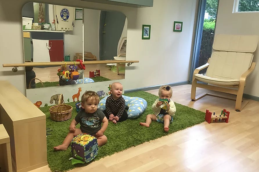 Three children sitting on a green rug in a room with a mirror