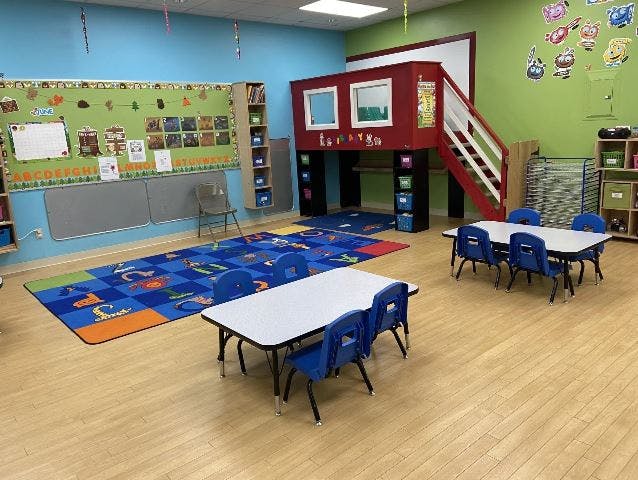 Classroom with small tables and chairs, a colorful rug, and a play structure