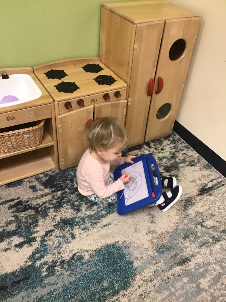 Child drawing on a magnetic sketch pad in a play kitchen area