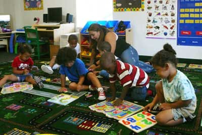 Adult and children playing with puzzles on a rug in a classroom