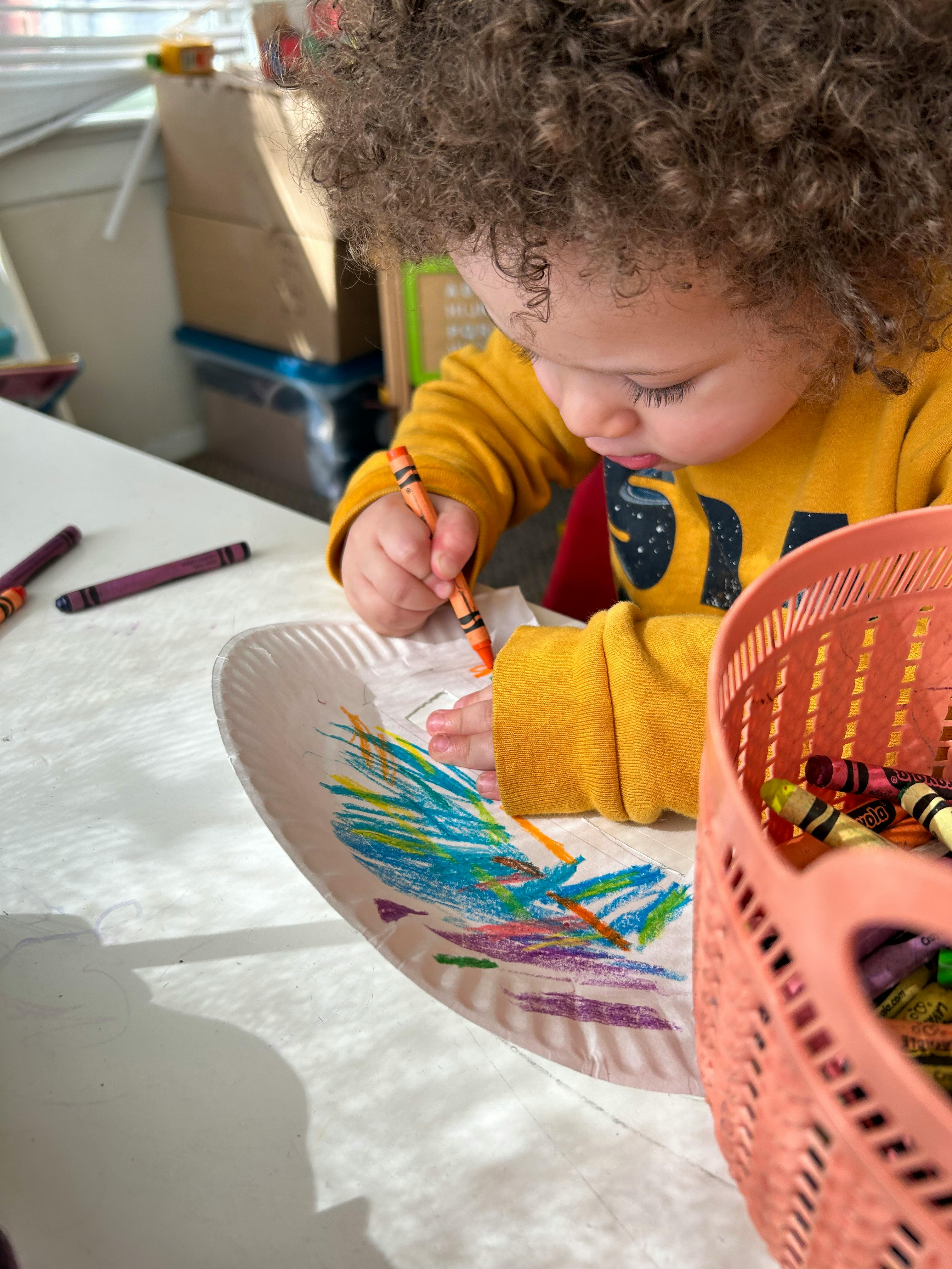 Child drawing on a paper plate with a crayon
