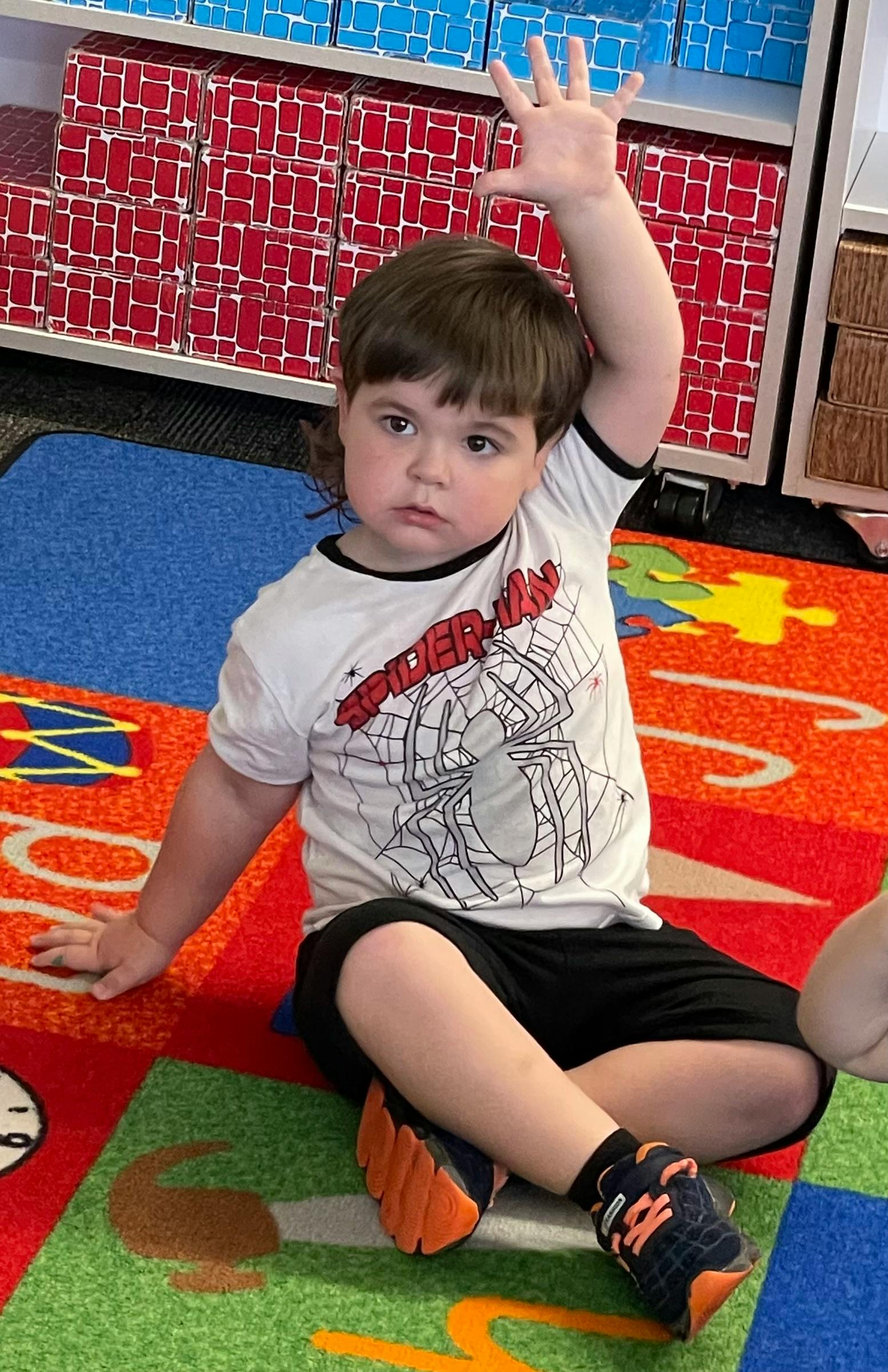 Child sitting on a colorful rug with one arm raised