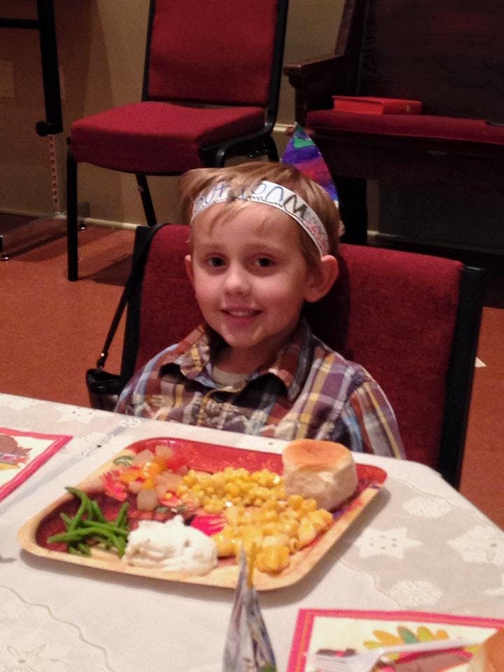 Child wearing a party hat and headband, sitting at a table with a plate of food