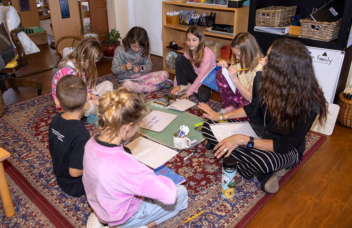 Adult and children sitting on a rug, working on papers