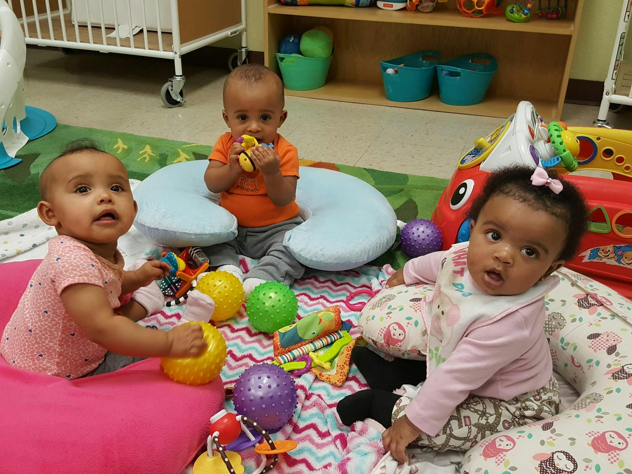 Three babies playing with toys on a colorful mat