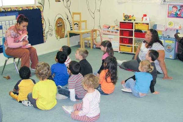 Two adults reading to a group of children in a classroom
