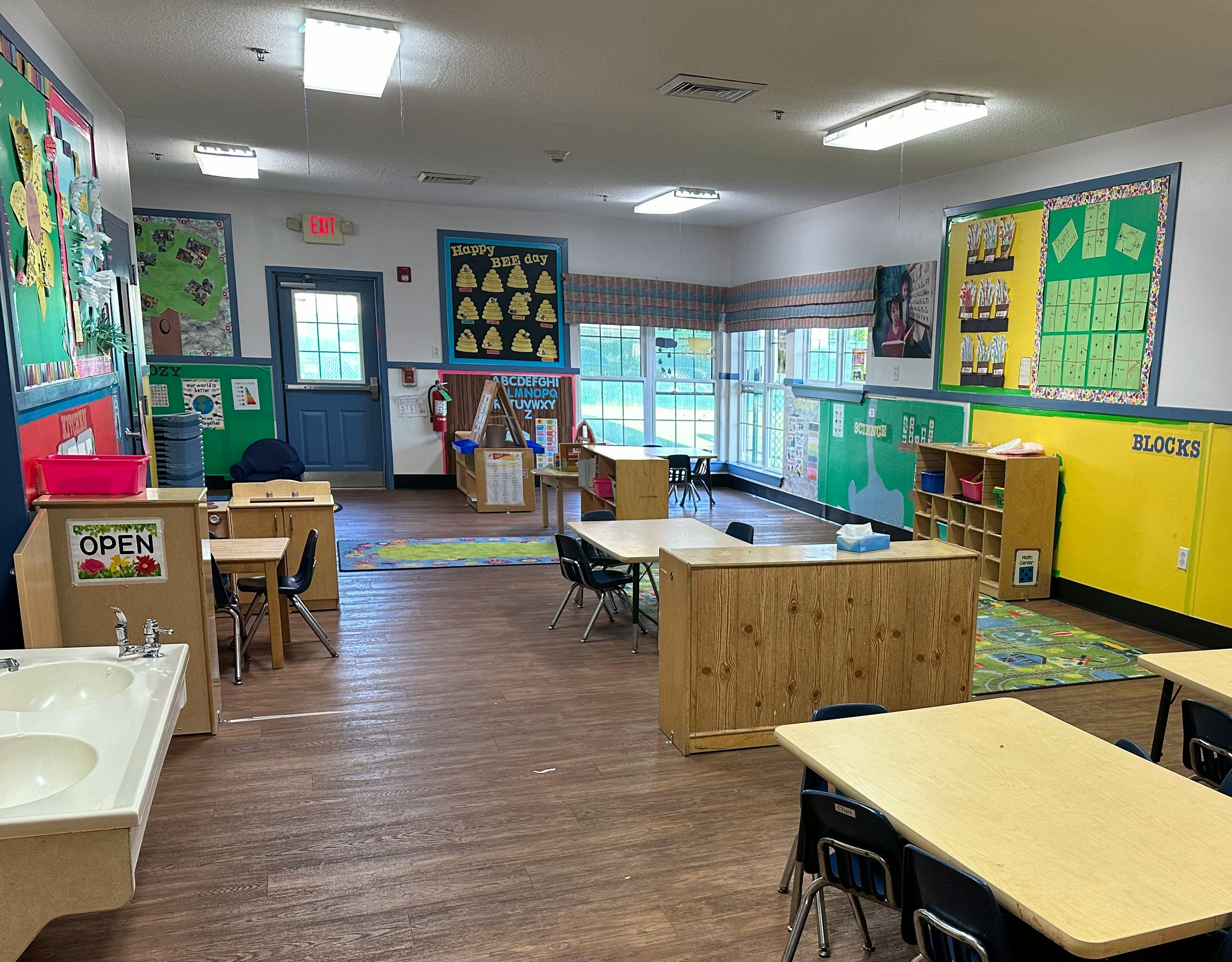Empty classroom with small tables and chairs, windows along one wall