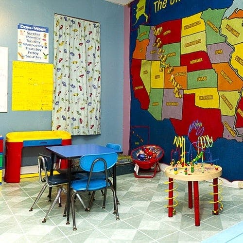 Children's classroom with small tables and chairs, toys, and a map on the wall