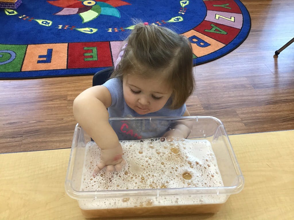 Child playing with bubbles in a clear container