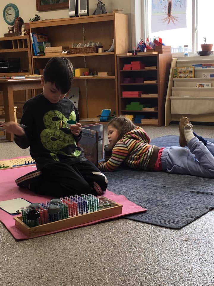 Child kneeling and holding an object, another child lying on a rug