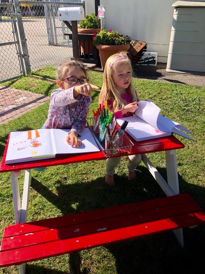 Two children drawing at a red picnic table outdoors